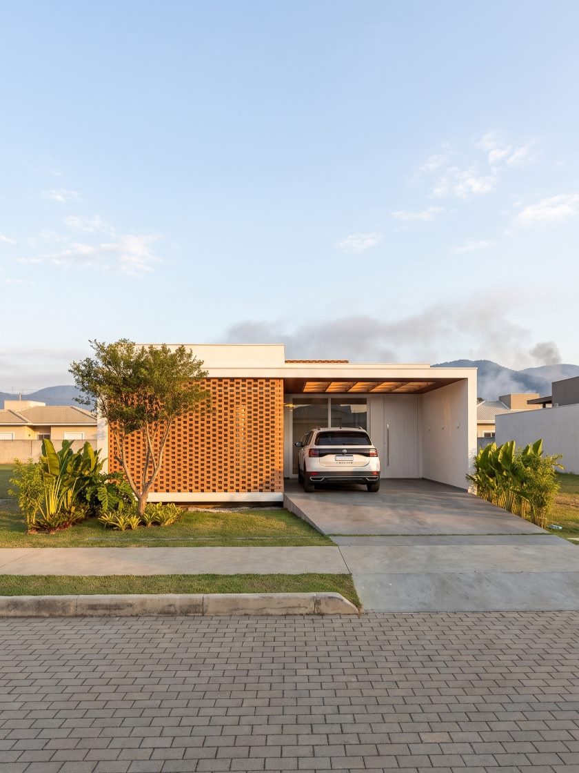 Fachada da Casa Brisa ao entardecer, com painel de cobogó cerâmico, carport integrado e paisagismo tropical